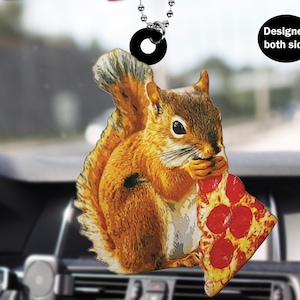 May include: A red squirrel with a bushy tail is holding a slice of pepperoni pizza in its paws. The squirrel is looking at the pizza and appears to be about to take a bite. The image is a car air freshener with a design on both sides.