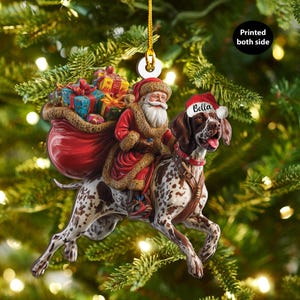 May include: A Christmas tree decoration showing Santa Claus riding a dog with a red collar and a Santa hat that says "Bella". Santa carries a sack of gifts. The ornament is printed on both sides.