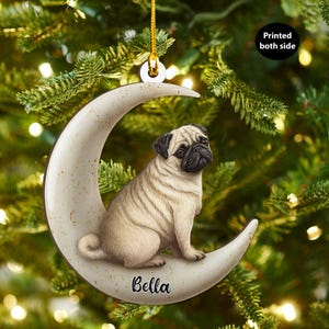 Puede incluir: Adorno de Navidad de un pug beige sentado en una luna creciente. El adorno tiene una cuerda dorada para colgar y el nombre "Bella" está escrito en la luna. El adorno está impreso por ambas caras.
