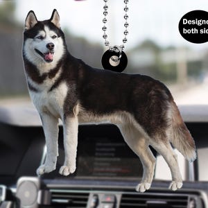 Könnte beinhalten: Ein schwarzer und weißer Husky-Hunde-Anhänger für das Auto, der an einer silbernen Kette mit einem schwarzen runden Anhänger hängt. Der Anhänger ist so konzipiert, dass er auf beiden Seiten angezeigt werden kann.