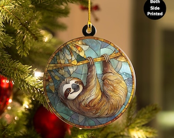 May include: Round Christmas ornament featuring a sloth hanging from a branch, designed in a stained-glass style. The ornament has a gold hanging string and the text "Both Side Printed". The background is a mix of blue and green.