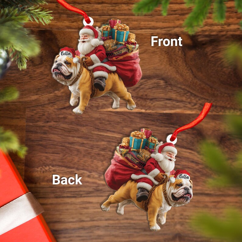 Pu&ograve; includere: Un ornamento natalizio con Babbo Natale che cavalca un bulldog, trasportando un sacco di regali. Il bulldog indossa un cappello da Babbo Natale con il nome "Bella". L'ornamento ha un nastro rosso per appenderlo, su sfondo di legno.