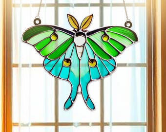 May include: A stained glass window hanging featuring a green and blue luna moth with intricate details. The moth is hanging from a silver chain.