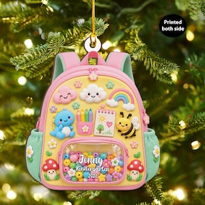 Puede incluir: Un adorno navideño con forma de mochila en color amarillo y rosa, con un bolsillo frontal transparente lleno de cuentas de colores. El adorno muestra el texto Jenny Kindergarten 2026 e incluye gráficos de un dinosaurio azul, una abeja, un arcoíris, nubes y setas. Impreso por ambas caras.