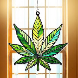 Peut inclure: Un vitrail suspendu représentant une feuille de marijuana verte avec des accents jaunes et bleus.