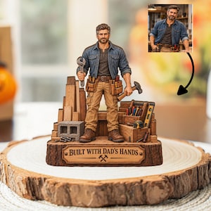 Pode incluir: Uma estatueta personalizada de um homem barbudo com camisa jeans e calças de trabalho bege, segurando uma chave inglesa e um martelo. A base é uma placa com textura de madeira com o texto "BUILT WITH DAD'S HANDS" e ícone de martelos cruzados.