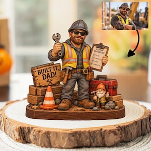 May include: A figurine of a construction worker with a beard and sunglasses, wearing a hard hat and high-visibility vest. The worker holds a wrench and a clipboard labelled SAFETY CHECKLIST. A small gnome, a toolbox, and a sign reading BUILT IT, DAD! are included.