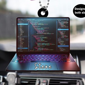 Op de afbeelding: Een zwarte laptop met een scherm dat code weergeeft, een toetsenbord en een trackpad. De laptop heeft een rood en blauw verloopseffect. De naam "Steve" staat op het trackpad. De laptop hangt aan een zwarte ketting.