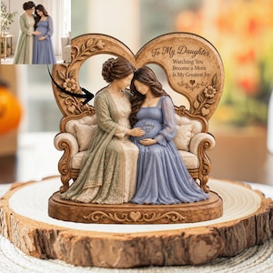 May include: A decorative figurine featuring two figures sitting on a sofa within a heart-shaped wooden frame. The frame is engraved with the text To My Daughter, Watching You Become a Mom Is My Greatest Joy. One figure wears a sage green dress, and the other wears a blue dress with the name Jenny and a heart symbol on the bodice.