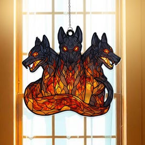 May include: A stained glass Cerberus ornament, depicting three black dog heads with glowing orange eyes and fiery orange and yellow flames. The ornament hangs from a silver chain, ideal for Halloween or gothic decor.