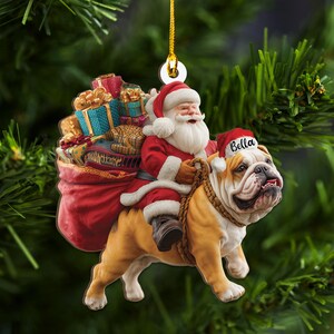 Pu&ograve; includere: Un ornamento natalizio con Babbo Natale su un bulldog. Babbo Natale indossa un abito e un cappello rossi, con un sacco di regali. Il bulldog indossa un cappello da Babbo Natale con il nome "Bella". L'ornamento &egrave; appeso a un filo d'oro.