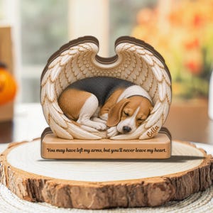 Può includere: Una statuetta commemorativa raffigurante un cucciolo di beagle addormentato accoccolato tra un paio di ali d'angelo scolpite. La base è incisa con il nome Bella e il testo: You may have left my arms, but you'll never leave my heart.