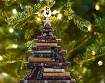 May include: A Christmas tree ornament shaped like a stack of books. The ornament is brown with a star on top and snowflake accents. The books are various colors, including red, brown, and black. A gold string is attached for hanging.