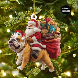 Pu&ograve; includere: Un ornamento natalizio con Babbo Natale che cavalca un bulldog. Babbo Natale indossa un abito e un cappello rossi e il bulldog indossa un cappello da Babbo Natale con il nome "Bella". Un sacco rosso di regali &egrave; dietro Babbo Natale. Il testo "Printed both side" &egrave; sull'ornamento.