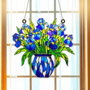 Peut inclure: Une fenêtre en verre coloré suspendue avec un vase bleu et blanc rempli de fleurs d'iris bleues et violettes.