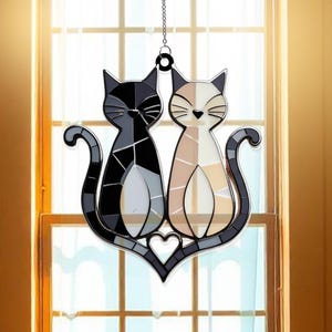 Op de afbeelding: Een zonvanger van gekleurd glas met twee katten, een zwarte en een witte, met een hart in het midden. De katten kijken elkaar aan en hun staarten zijn in elkaar gevlochten.