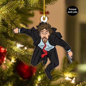 May include: A Christmas ornament featuring a cartoon illustration of a man in a suit jumping with a gun in his hand. The ornament is printed on both sides.
