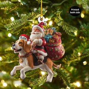Peut inclure: Ornement de Noël représentant le Père Noël sur un chien beagle. Le Père Noël porte un costume et un chapeau rouges, avec une barbe blanche et un sac de cadeaux. Le chien est marron, blanc et noir, avec un chapeau de Père Noël avec le mot "Bella".