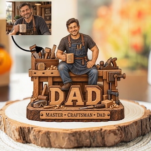 Könnte beinhalten: Eine Figur eines lächelnden Handwerkers, der auf einer Werkbank sitzt und eine Tasse mit der Aufschrift GOOD TOOLS BETTER DAYS hält. Der Sockel zeigt das Wort DAD und ein Schild mit MASTER CRAFTSMAN DAD. Inklusive Werkzeugen und Holzspänen.