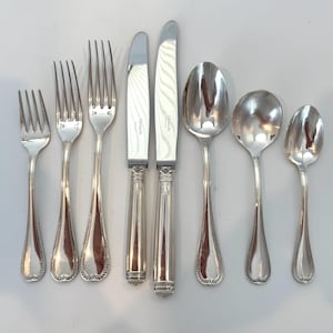 May include: A set of seven silver-toned metal utensils including three forks of varying sizes, two knives with smooth blades, and two spoons of different sizes. Each piece features a decorative beaded pattern at the base of the handle.