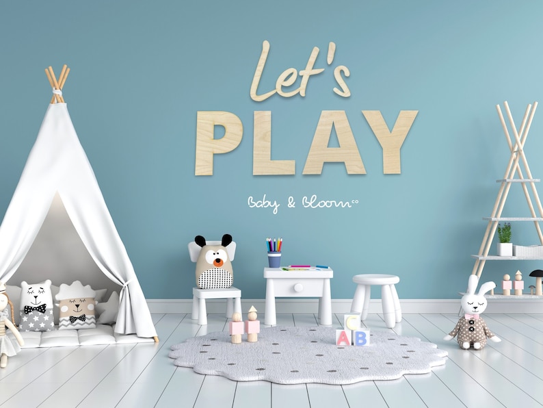 May include: A light blue room with a white teepee tent, a wooden table and chairs, and a rug with black dots. The wall has wooden letters spelling "Let's Play" with the text "Baby & Bloom Co." below.