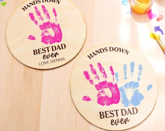 May include: Two round wooden plaques with handprints in pink and blue paint. The plaques say "Hands Down Best Dad Ever" with a personalized name.