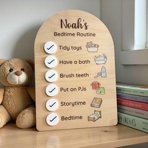 May include: A wooden bedtime routine chart, arched at the top, with "Noah's Bedtime Routine" written on it. The chart has illustrations for each step, including "Tidy toys," "Have a bath," and "Bedtime." A teddy bear is visible on the left.