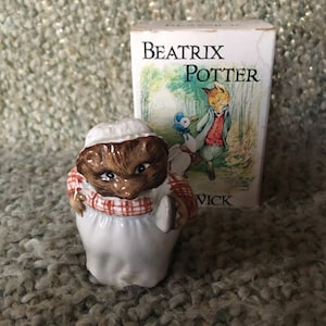 May include: A Beatrix Potter figurine of Mrs Tiggy-Winkle, a hedgehog wearing a red and white checked apron and a white cap, holding a metal pan. The figurine is standing on a brown carpet. The box for the figurine is in the background and features a picture of Peter Rabbit and a duck.