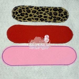 May include: Three fabric patches in the shape of an oval. The top patch is brown with a leopard print. The middle patch is red. The bottom patch is pink.