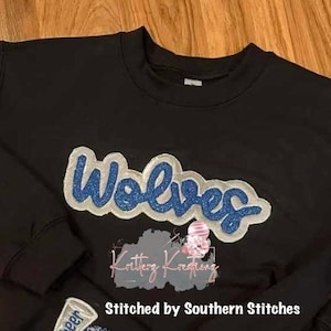 May include: Black sweatshirt with a blue and white glitter "Wolves" applique. The sweatshirt is stitched by Southern Stitches.