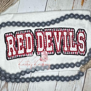 May include: White t-shirt with the words "RED DEVILS" in red, black, and white checkered fabric with white stripes. The letters are outlined in black.