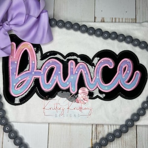 Può includere: Una maglietta bianca con un design "Dance" nero e rosa con pois bianchi e un effetto ombré arcobaleno. Il design è contornato di nero e ha una finitura lucida.