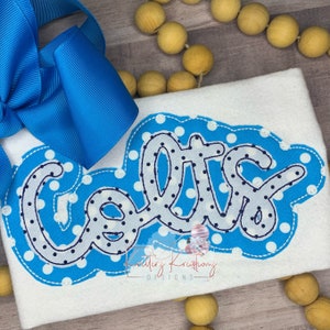 May include: A white shirt with a blue and white polka dot design. The word "Cole" is written in a blue and white script font with a gray outline.