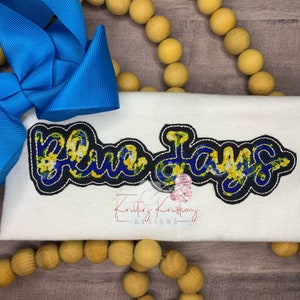 Può includere: Maglietta bianca con un ricamo blu e giallo che dice "Blue Jays".