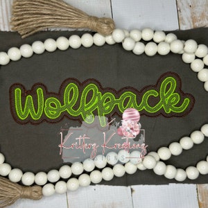 Könnte beinhalten: Grüner gestickter "Wolfpack"-Text auf braunem Stoffhintergrund mit weißen Perlen und einem braunen Quasten.