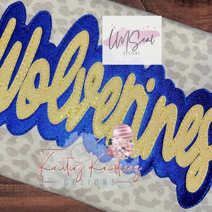 Puede incluir: Un diseño de planchado con purpurina dorada con la palabra "Wolverine" en un contorno azul. El diseño está sobre una tela blanca con estampado de leopardo.