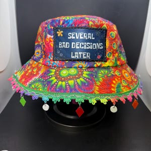 May include: A colorful bucket hat with a psychedelic print and a patch that reads "Several Bad Decisions Later".