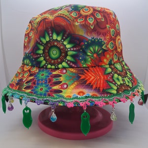 May include: A colorful bucket hat with a psychedelic print and a green trim. The hat has a beaded fringe with green charms.