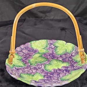 May include: A ceramic serving dish with a grapevine design. The dish has a raised rim and a handle made of natural bamboo.