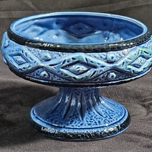 Op de afbeelding: Een blauwe keramische voetkom met een zwarte rand en een geometrisch ontwerp. De kom heeft een getextureerd oppervlak en een brede basis.