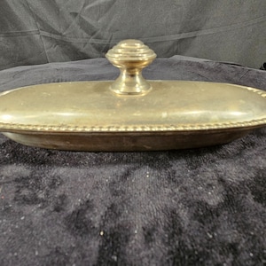 Könnte beinhalten: Eine ovale silberne Schale mit Deckel und einem dekorativen Knopf oben. Die Schale hat einen perlenbesetzten Rand.