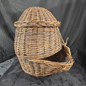 Könnte beinhalten: Ein brauner Weidenkorb mit Deckel. Der Korb ist oval geformt und hat ein geflochtenes Design. Der Deckel ist leicht geöffnet und gibt den Blick ins Innere des Korbes frei.