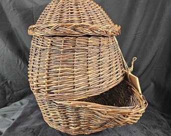 May include: A brown wicker basket with a lid. The basket is oval shaped and has a woven design. The lid is slightly ajar, revealing the inside of the basket.