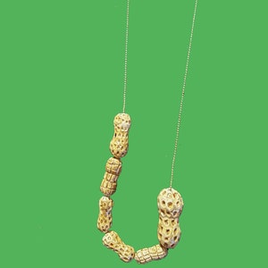 Puede incluir: Un collar hecho de cáscaras de cacahuete enhebradas en una cadena plateada. Las cáscaras de cacahuete son de color marrón claro y tienen una superficie texturizada.