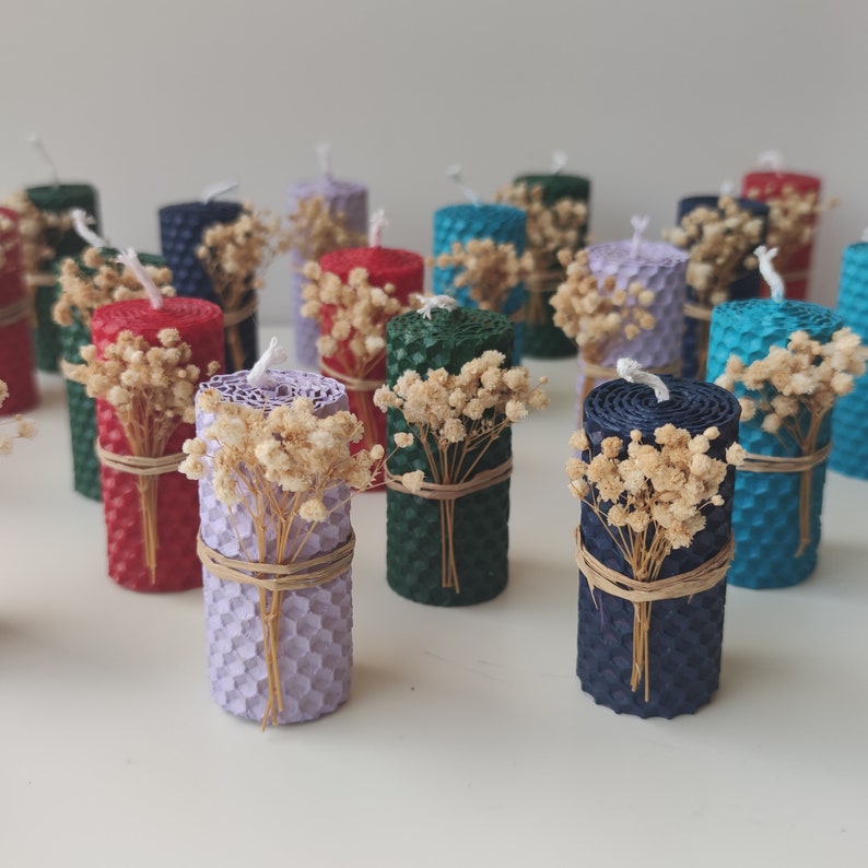 May include: Assortment of small, colorful, honeycomb-shaped candles with dried flowers. The candles are arranged on a white surface.