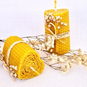 May include: Two natural beeswax candles, one is a honeycomb design and the other is a spiral design. Both candles are decorated with dried white flowers.