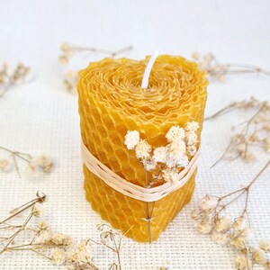 May include: A yellow honeycomb candle with a white wick and a natural twine band. The candle is decorated with small white flowers.