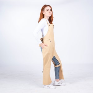 May include: A tan canvas apron with adjustable straps and a leg strap. The apron has a large pocket on the front and a slit on the side for easy access.