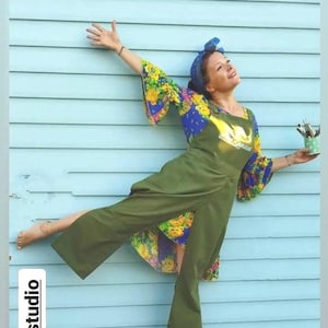 Puede incluir: Mono verde oliva con perneras anchas y top con estampado floral. Las mangas son acampanadas con un diseño floral azul y amarillo. También se ve un pañuelo azul y un pequeño recipiente verde con pinceles.