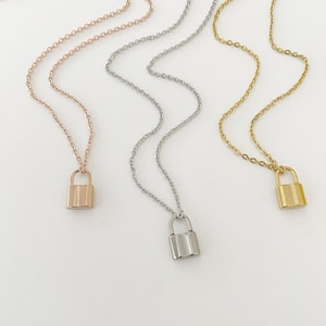 May include: Three delicate necklaces with padlock pendants. The necklaces are silver, gold, and rose gold.